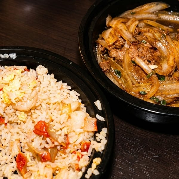Two black bowls of Asian food, one with fried rice and the other with beef and onions.