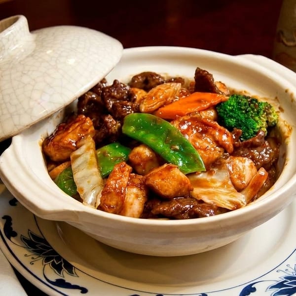 Clay pot with beef, chicken, broccoli, carrots, and snow peas on a patterned plate.