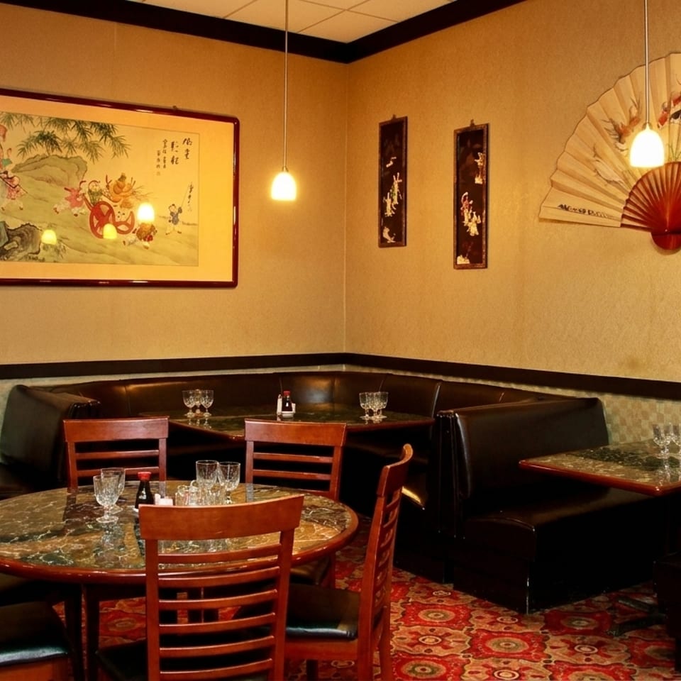 Cozy restaurant interior with dark booths, round tables, and Asian-inspired art on light yellow walls.
